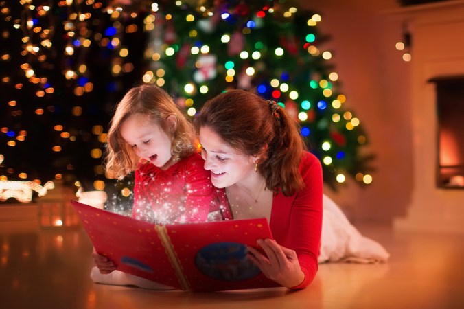 Mother And Daughter Reading At Fire Place On Christmas Eve