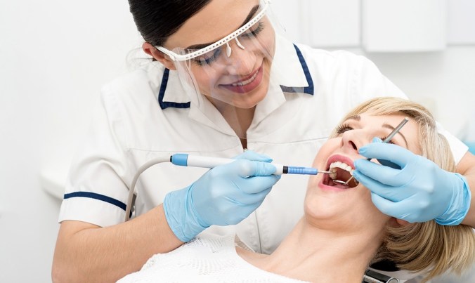 Smiling female dentist procedure of teeth cleaning